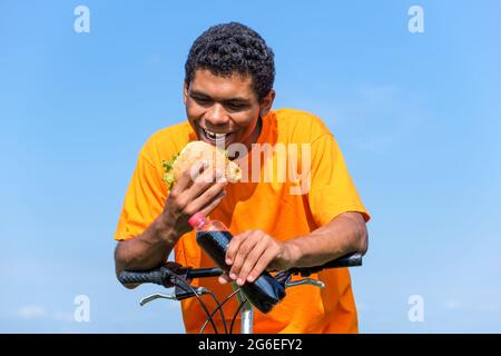 Afroamerikanischer Mann genießt den Geschmack von Hamburger und Cola-Getränk im Freien Stockfoto
