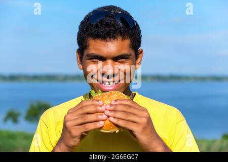 Afroamerikanischer Mann, der den Geschmack eines Hamburgers im Freien genießt Stockfoto