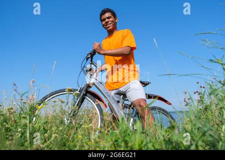 Afroamerikanischer Mann, der mit dem Fahrrad auf der Wiese gegen den blauen Himmel steht Stockfoto