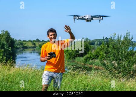 Afroamerikanischer Mann, der Drohne mit Controller in Händen auf der Wiese betreibt Stockfoto