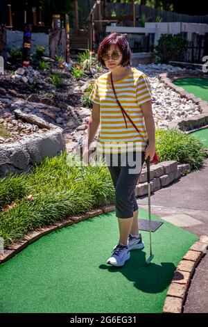 Osage Beach, MO – 21. Juni 2021; Asiatin, die mit dem Putter in der Hand auf dem Green Turn auf dem Minigolfplatz im Lake of ozarks läuft Stockfoto