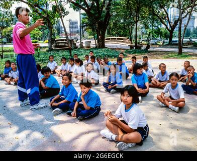 Lehrer und Klasse von Schulkindern, die eine Lektion im Lumphini Park, Bangkok, Thailand, haben Stockfoto