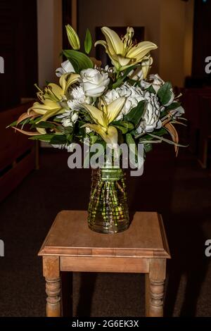 Schöner Blumenstrauß mit gelben Lilien und weißen Rosen in einer Glasvase auf einem Holztisch. Stockfoto