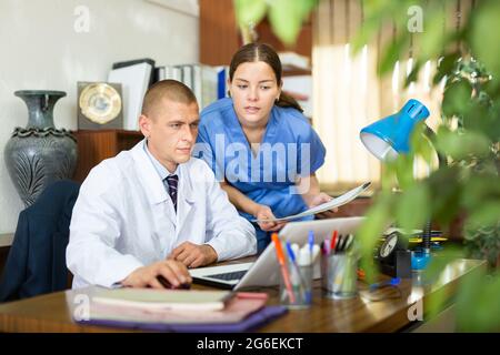 Junge Kollegen-Ärzte diskutieren die Verabredung der Behandlung, sitzen am Computer im Büro Stockfoto