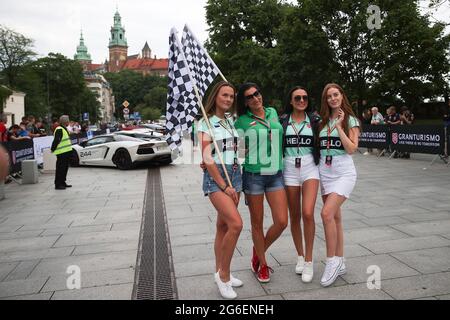 Krakau, Polen. Juli 2021. Während des Gran Turismo Polonia in Krakau posieren Frauen vor einer Linie der exklusiven Autos, die eine Rennflagge halten. In Krakau fand die größte Supersportmesse Polonia, Gran Turismo Polonia, statt. Über 100 Fahrzeuge (z. B. Ferrari, Porsche, Lamborghini) wurden während der 17. Ausgabe der Veranstaltung in der Nähe des Sheraton Gran Hotels geparkt. Der Wert der Autos, die an der Versammlung teilgenommen haben, wurde auf 120 000 000 PLN geschätzt. Kredit: SOPA Images Limited/Alamy Live Nachrichten Stockfoto