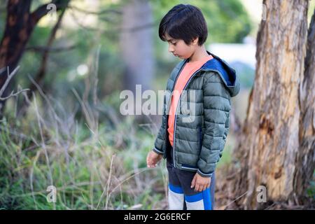 Einsamer Junge, der das Gras berührt. Porträt eines Kindes im Freien bei natürlichem Licht. Natürliche Umgebung, Einsamkeit. Stockfoto