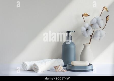 Badezimmereinrichtung in beigefarbenen Pastelltönen. Weißes Regal im Badezimmer mit Handtüchern, Seife, Shampoo-Flasche, Zimmerpflanze. Modell mit Platz für Text. Minimale Kommunikation Stockfoto