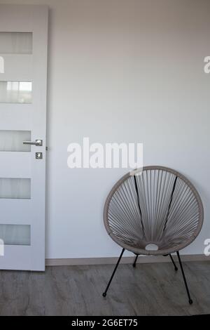 Ein Teil des Zimmers mit Cappuccino-Stuhl, weißer Wand, grauem Boden und weißer Tür Stockfoto