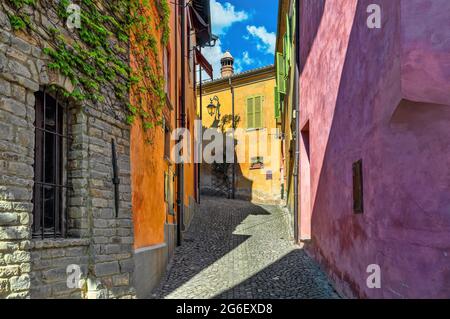 Enge gepflasterte Straße zwischen alten bunten Häusern in der kleinen Stadt Monforte d'Alba im Piemont, Norditalien. Stockfoto