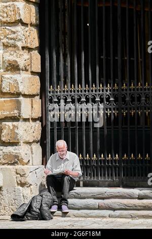 Ein älterer Mann sitzt vor dem Radcliffe Camera Gebäude der Bodleian Bibliothek, Universität Oxford, England, beim Lesen einer Zeitung. Stockfoto