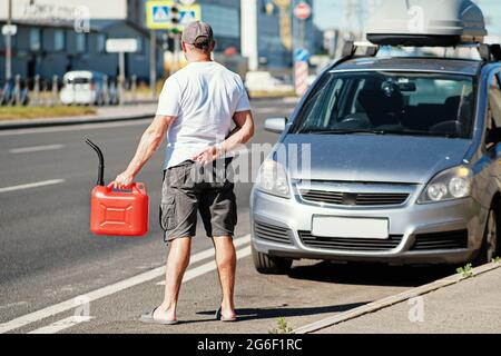 Ein roter Kanister auf dem Asphalt in der Nähe des Autos. Das Auto hatte kein Benzin mehr und war zum Stillstand gekommen. Ein junger Mann, der auf Hilfe von anderen Fahrern hofft Stockfoto