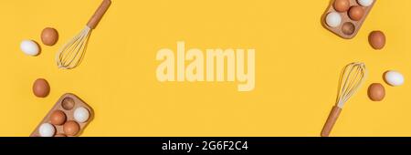 Banner mit Eiern in Holzeierkasten und Schneebesen auf gelbem Hintergrund. Flach liegend Draufsicht Kopierbereich. Stockfoto