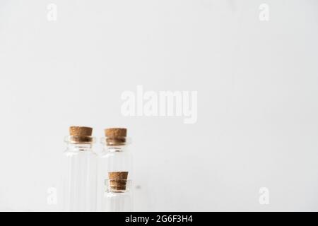 Drei Glasflaschen mit Korkstopfen auf Holzpodium mit weißem Wandhintergrund. Nachfülllager für ätherisches Öl. Modup-Vorlage. Stockfoto