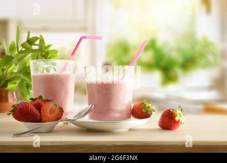 Gläser voller Erdbeer-Smoothie auf einem Holztisch voller Früchte in der Küche. Vorderansicht. Stockfoto