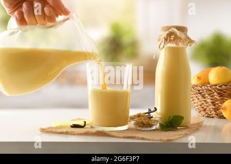 Hand mit Krug voller Vanillemilch, serviert in einem Glas auf der Küchenbank. Vorderansicht. Stockfoto