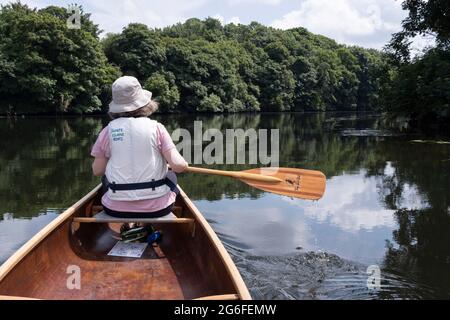 Die Rückansicht einer Kanufahrerin, die am 2. Juli 2021 in Norwich, Norfolk, England, auf dem Fluss Yare in der Nähe von Thorpe St. Andrew paddelt. Stockfoto