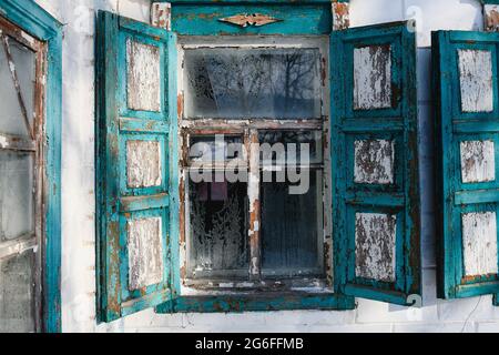 Holzfensterrahmen des alten ukrainischen Landhauses mit strukturierter Farbe und offenen Fensterläden im Winter weißen Frost hoar Stockfoto