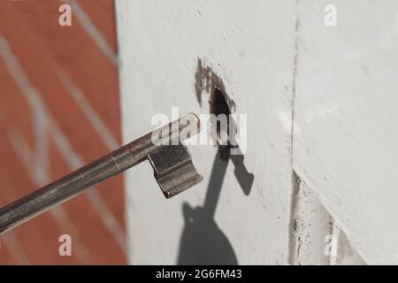 Einfacher, eiserner Türschlüssel zum Schlüsselloch einer weißen Scheunentür. Juli, Niederlande. Stockfoto