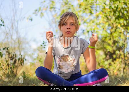 Defocus caucasian preteen Mädchen praktiziert Yoga im Park, Wald, im Freien, draußen. Meditation und Konzentration. Wellness gesunder Lebensstil. Hochformat o Stockfoto