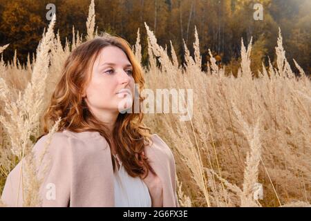 Eine Erwachsene Frau in einer beigen Jacke geht im Herbstgras in der Natur spazieren Stockfoto