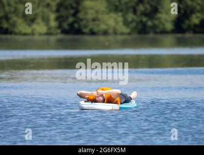 Anonymer Mann, der auf dem Float-Board schläft und im See schwimmt, schläft schnell. Aufblasbares Surfboot auf ruhigem Wasser. Stockfoto