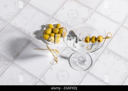 Martini-Cocktail mit Oliven auf dem gefliesten Tisch. Ein alkoholischer Klassiker mit Eis in einem eleganten Glas Stockfoto
