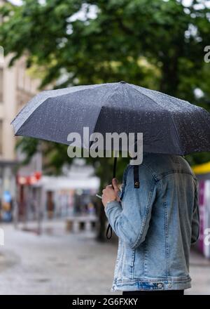 Schutz vor dem starken Sturmregen unter einem Regenschirm mit herunterlaufenden Wasserperlen. Telefoniert stand im Einkaufsviertel der Innenstadt. Stockfoto