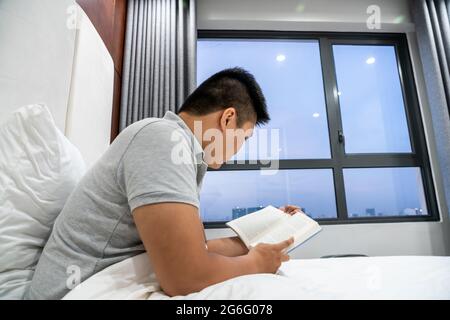 Seitenansicht des Mannes, der Buch auf dem Bett las Stockfoto