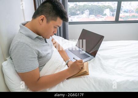 Seitenansicht eines jungen Mannes, der Notizen auf dem Bett schrieb Stockfoto