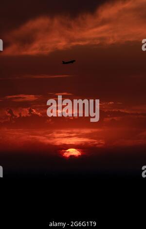 Das Flugzeug hebt vor dem Hintergrund eines roten Himmels und eines wunderschönen Sonnenuntergangs ab. Silhouette eines Flugzeugs über der Sonne Stockfoto