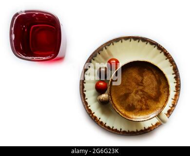 Türkischer Kaffee auf weißem Hintergrund und Vorderseite. Farbige Schokolade neben dem Kaffee und Wasser in einem roten Glas. Stockfoto