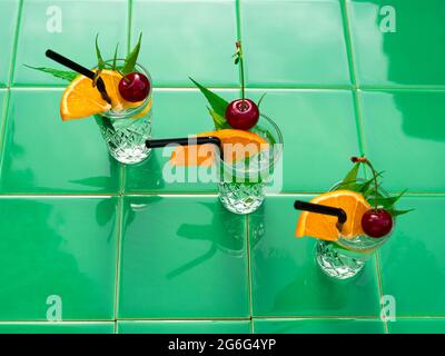 Erfrischende Getränke in Kristallgläsern grün Blätter kirschorange Scheibe Fliesen Hintergrund Schatten. Süßer, kalter natürlicher Cocktail an heißen Sommertagen. Sodawasser Stockfoto