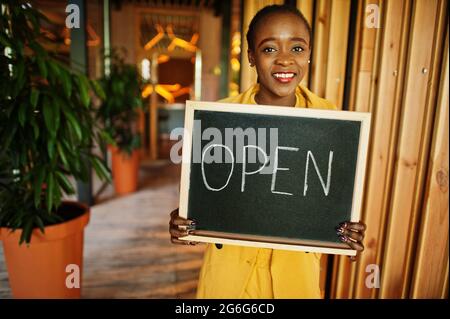 afroamerikanische Frau halten offene Willkommenstafel im modernen Café-Café-Café bereit, Service, Restaurant, Einzelhandelsgeschäft, Kleinunternehmerin. Stockfoto