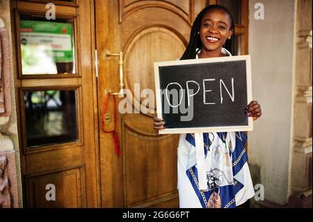 afroamerikanische Frau halten offene Willkommenstafel im modernen Café-Café-Café bereit, Service, Restaurant, Einzelhandelsgeschäft, Kleinunternehmerin. Stockfoto