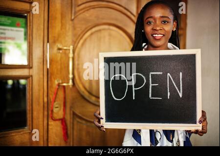 afroamerikanische Frau halten offene Willkommenstafel im modernen Café-Café-Café bereit, Service, Restaurant, Einzelhandelsgeschäft, Kleinunternehmerin. Stockfoto