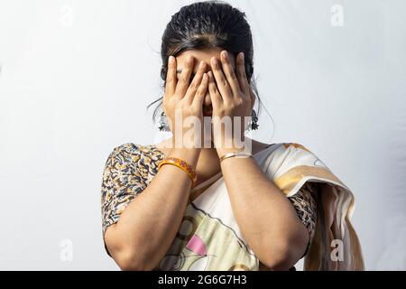 Isoliert auf weißem Hintergrund ein indisches weibliches Gesicht bedeckt mit Händen auf weißem Hintergrund Stockfoto