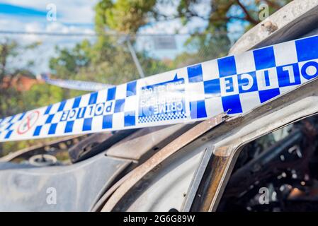 Polizeiband an einem bestimmten Tatort, umwickelt um ein ausgebranntes Auto in Sydney, New South Wales, Australien Stockfoto