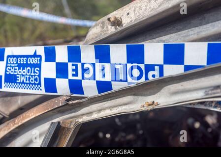 Polizeiband an einem bestimmten Tatort, umwickelt um ein ausgebranntes Auto in Sydney, New South Wales, Australien Stockfoto