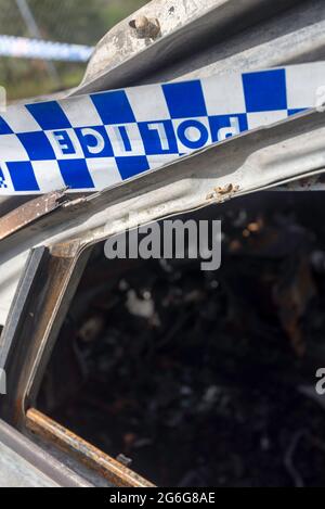 Polizeiband an einem bestimmten Tatort, umwickelt um ein ausgebranntes Auto in Sydney, New South Wales, Australien Stockfoto