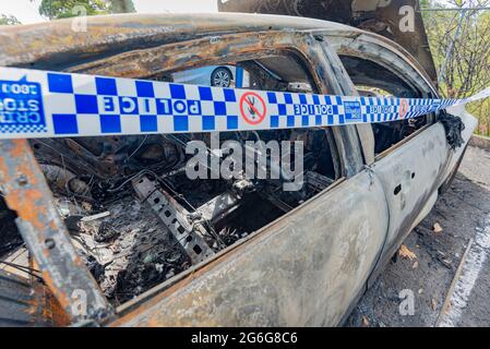 Polizeiband an einem bestimmten Tatort, umwickelt um ein ausgebranntes Auto in Sydney, New South Wales, Australien Stockfoto