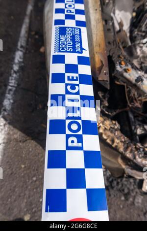 Polizeiband an einem bestimmten Tatort, umwickelt um ein ausgebranntes Auto in Sydney, New South Wales, Australien Stockfoto