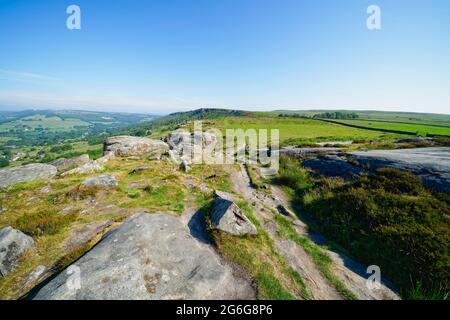 Ein unebener, schmaler Pfad schlängelt sich über den Baslow Edge in Richtung eines entfernten Curbar Edge an einem trüben Sommermorgen im Derbyshire Peak District. Stockfoto