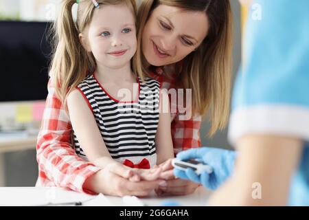 Der Arzt überprüft den Blutzuckerspiegel des kleinen Mädchens mit einem digitalen Glucometer im Krankenhaus Stockfoto