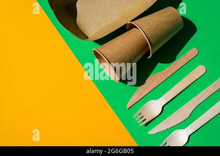Holzgabeln und Pappbecher mit Tellern auf farbigem Hintergrund. Umweltfreundliches Einweggeschirr. Wird in Fast Food, Restaurants, Imbissbuden und Picknicks verwendet. Nein Stockfoto