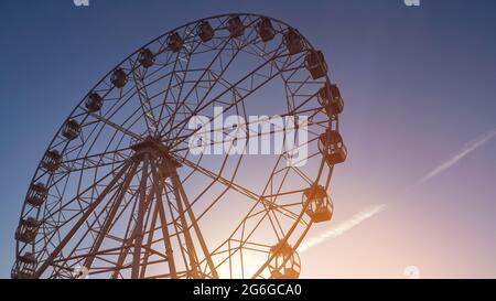 Am Frühlingsabend dreht sich im Park unter klarem blauen Himmel die große Fahrtfahrt mit dem Riesenrad aus Metall Stockfoto