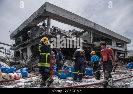 Bang Phli, Thailand. Juli 2021. Thailändische Feuerwehrleute stehen neben dem beschädigten Gebäude, das durch eine Explosion in einer von einem Brand heimgetragenen Ming Dih Chemical Fabrik im Bezirk Bang Phli, Provinz Samut Prakan, verursacht wurde.bei einer Explosion über Nacht und einem Brand in einer Chemiefabrik wurde eine Person getötet und mehr als 60 weitere verletzt. Am späten Montagnachmittag sendend schwarzer Rauch über Samut Prakans Bang Phli-Gebiet in den Himmel. Feuerwehrleute verwendeten Hubschrauber, darunter auch einige von der Armee, um flammhemmenden Schaum über den brennenden Ming Dih Chemical Co-Anlagenkomplex zu sprühen. Kredit: SOPA Images Limited/Alamy Live Nachrichten Stockfoto