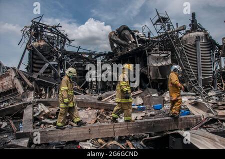 Bang Phli, Thailand. Juli 2021. Thailändische Feuerwehrleute gehen neben beschädigte Strukturen, die durch eine Explosion in einer von einem Brand heimgetragenen Ming Dih Chemical Fabrik im Bezirk Bang Phli, Provinz Samut Prakan verursacht wurden.bei einer Explosion über Nacht und einem Brand in einer Chemiefabrik wurde eine Person getötet und mehr als 60 weitere verletzt. Am späten Montagnachmittag sendend schwarzer Rauch über Samut Prakans Bang Phli-Gebiet in den Himmel. Feuerwehrleute verwendeten Hubschrauber, darunter auch einige von der Armee, um flammhemmenden Schaum über den brennenden Ming Dih Chemical Co-Anlagenkomplex zu sprühen. Kredit: SOPA Images Limited/Alamy Live Nachrichten Stockfoto