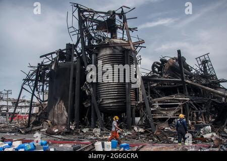 Bang Phli, Thailand. Juli 2021. Thailändische Feuerwehrleute gehen neben einen beschädigten Tank, der durch eine Explosion in einer von einem Brand heimgetragenen Ming Dih Chemical Fabrik im Bezirk Bang Phli, Provinz Samut Prakan, verursacht wurde.bei einer Explosion über Nacht und einem Brand in einer Chemiefabrik wurde eine Person getötet und mehr als 60 weitere verletzt. Am späten Montagnachmittag sendend schwarzer Rauch über Samut Prakans Bang Phli-Gebiet in den Himmel. Feuerwehrleute verwendeten Hubschrauber, darunter auch einige von der Armee, um flammhemmenden Schaum über den brennenden Ming Dih Chemical Co-Anlagenkomplex zu sprühen. Kredit: SOPA Images Limited/Alamy Live Nachrichten Stockfoto