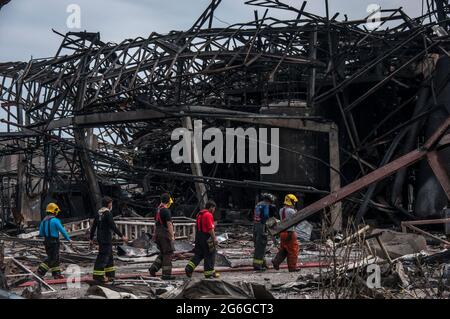 Bang Phli, Thailand. Juli 2021. Thailändische Feuerwehrleute gehen neben beschädigte Strukturen, die durch eine Explosion in einer von einem Brand heimgetragenen Ming Dih Chemical Fabrik im Bezirk Bang Phli, Provinz Samut Prakan verursacht wurden.bei einer Explosion über Nacht und einem Brand in einer Chemiefabrik wurde eine Person getötet und mehr als 60 weitere verletzt. Am späten Montagnachmittag sendend schwarzer Rauch über Samut Prakans Bang Phli-Gebiet in den Himmel. Feuerwehrleute verwendeten Hubschrauber, darunter auch einige von der Armee, um flammhemmenden Schaum über den brennenden Ming Dih Chemical Co-Anlagenkomplex zu sprühen. Kredit: SOPA Images Limited/Alamy Live Nachrichten Stockfoto