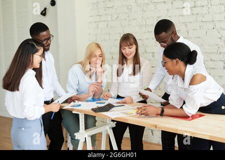 Ein Team aus multiethnischen Personen diskutiert im Büro über Geschäfte. Die Mitarbeiter des Unternehmens kommunizieren, betrachten die Zeitpläne und diskutieren Stockfoto